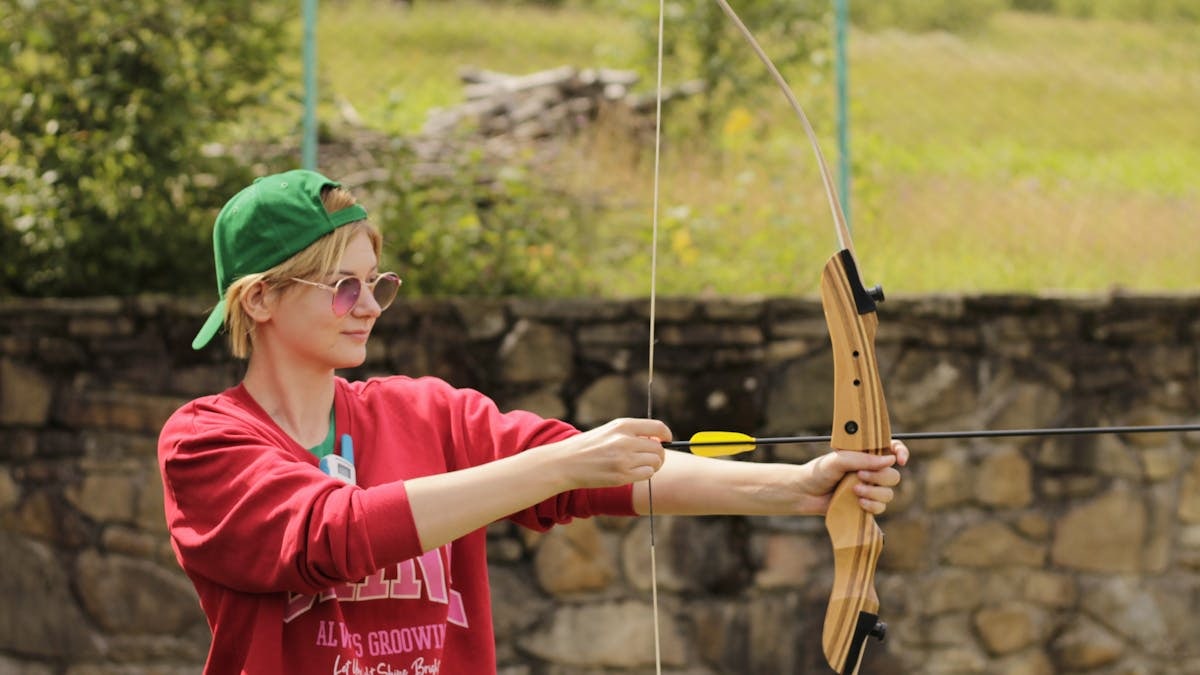 A young adult practicing archery outdoors in a casual setting, focusing on technique.